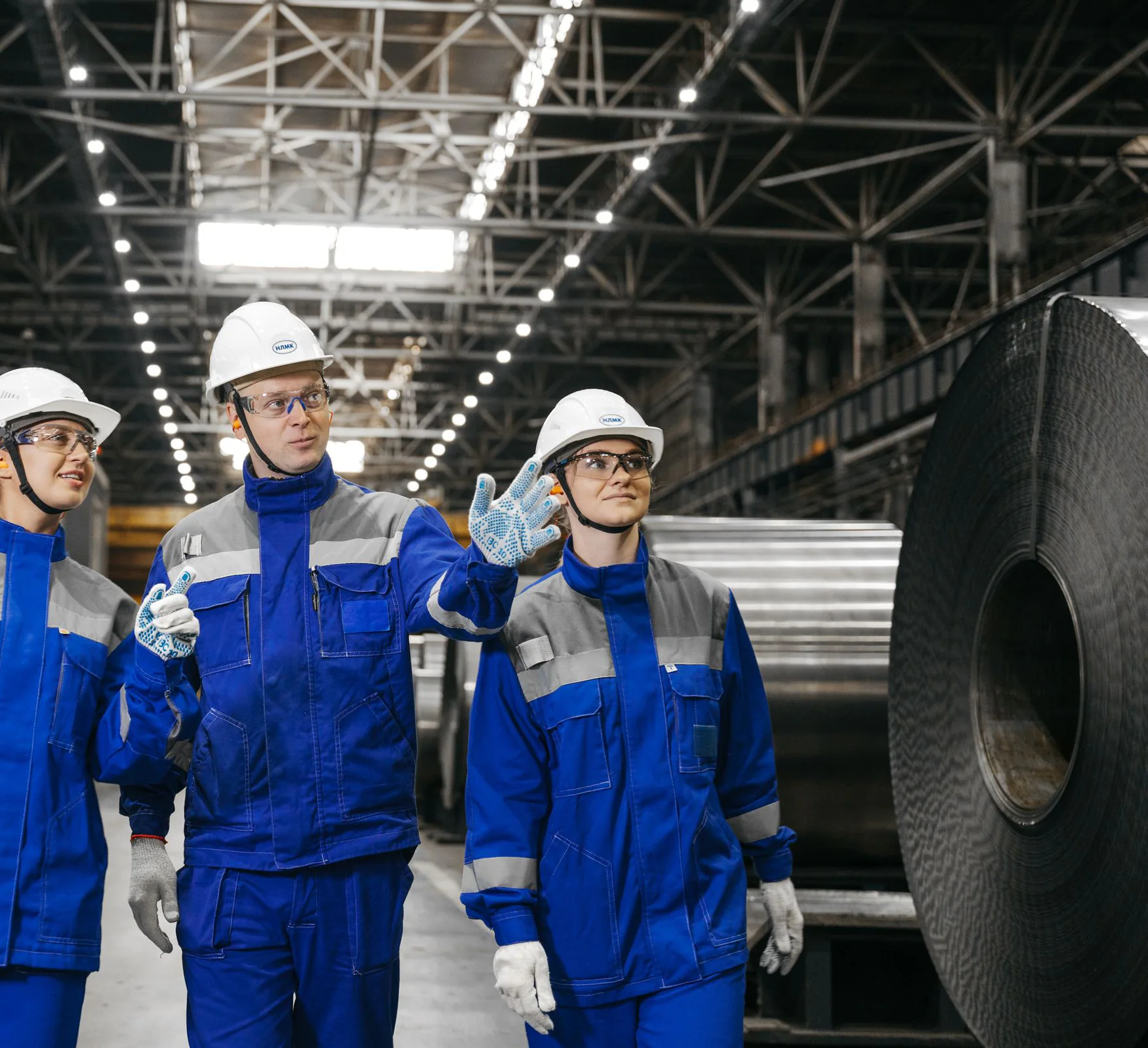 Industrial workers in protective equipment discussing work inside a manufacturing facility.